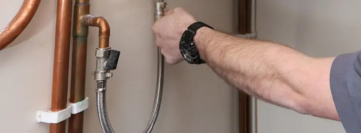 Hand adjusting a boiler filling loop connected to copper pipes.