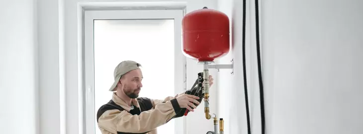 Engineer inspecting a red expansion vessel on a domestic heating system.