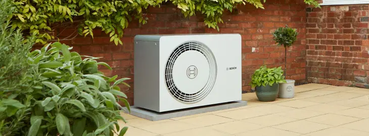 Bosch air source heat pump unit installed in a garden against a brick wall