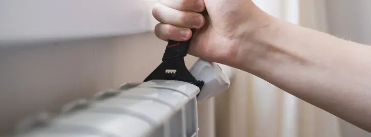 Person using a radiator key to bleed trapped air from a home radiator.