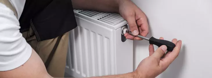 Engineer bleeding air from a household radiator to restore heating circulation.