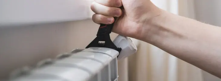 Person bleeding a radiator with a wrench to reduce boiler pressure