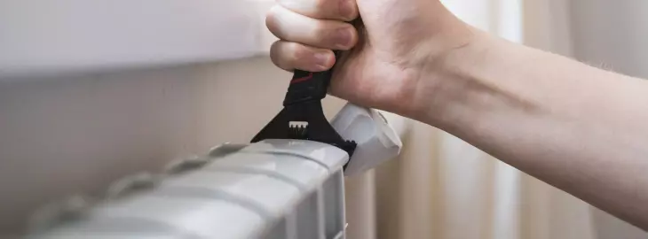 Person using a radiator key to bleed a radiator and release trapped air
