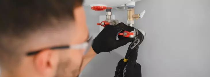 Engineer tightening a boiler’s filling loop valve to ensure it is fully closed.