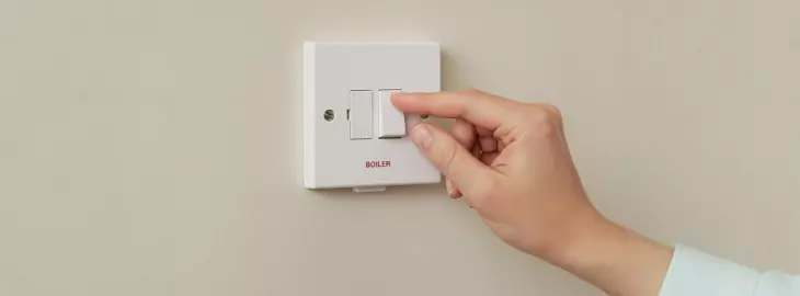 Hand switching the boiler isolation switch on a wall-mounted fuse spur