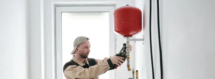 Heating engineer checking a red expansion vessel with tools on a wall-mounted system.