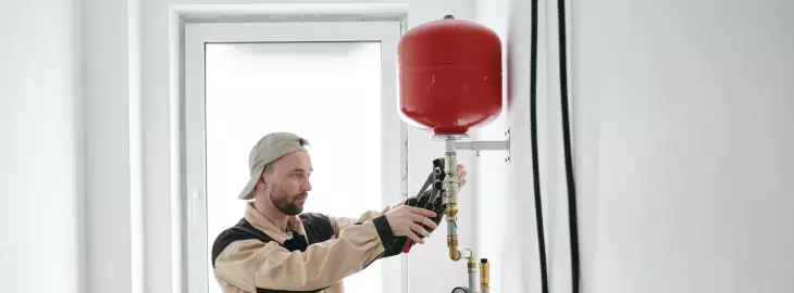 Engineer working on red expansion vessel connected to heating system