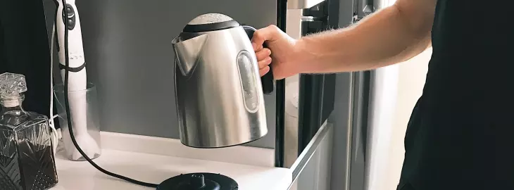 Person lifting an electric kettle in a kitchen, showing daytime electricity use