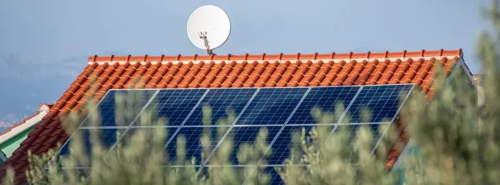 Roof with solar panels and satellite dish partially hidden by trees