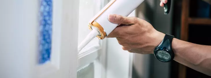 Person sealing gaps around a window frame with a caulking gun to reduce heat loss