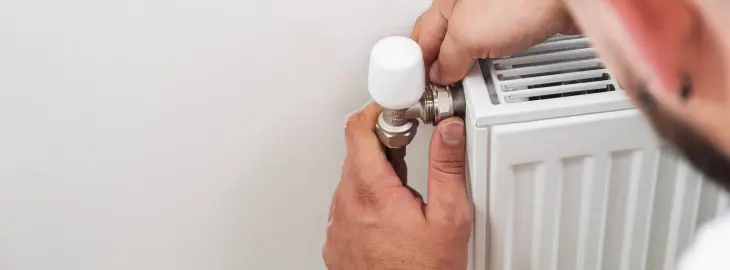 Person adjusting radiator valve during home heating check