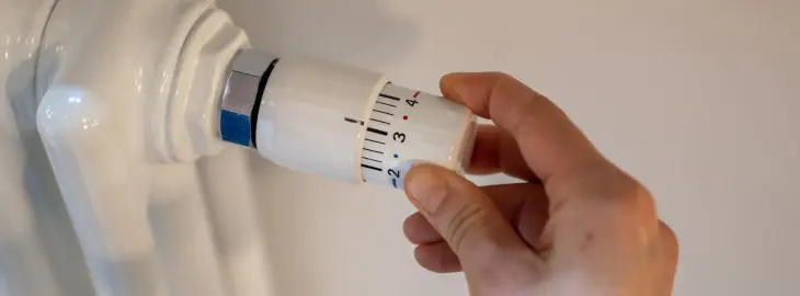 Person adjusting a thermostatic radiator valve (TRV) on a home radiator to control heating temperature.