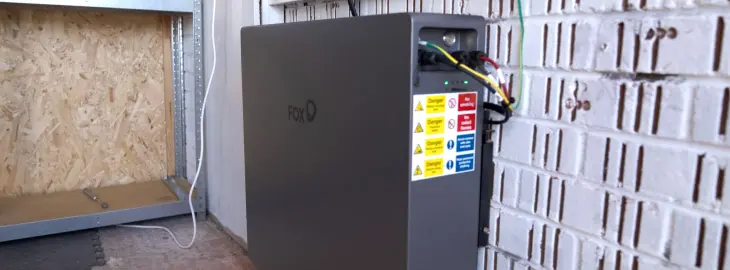Home battery storage unit installed in a garage with visible wiring and labels